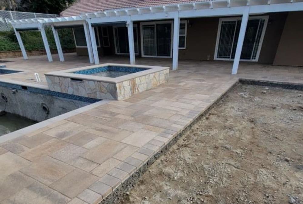 Backyard patio renovation featuring stone pavers, spa area, and unfinished landscaping.