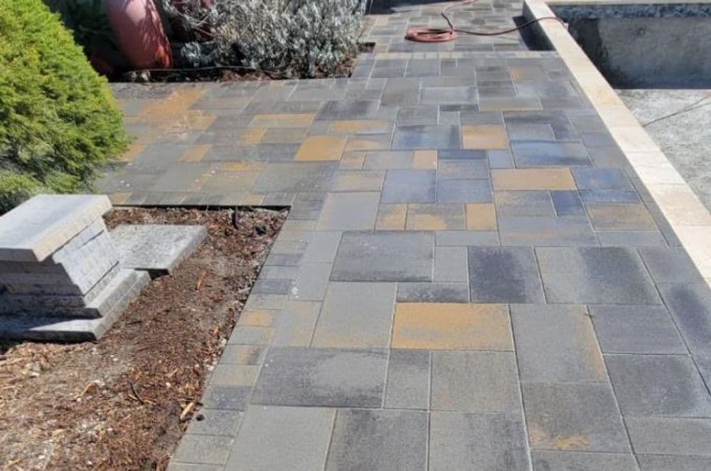 Paved walkway with grey stones and greenery, recently installed and clean.