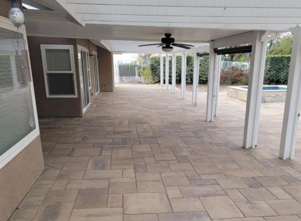 Outdoor patio with stone flooring, ceiling fan, and a view of a pool beyond.