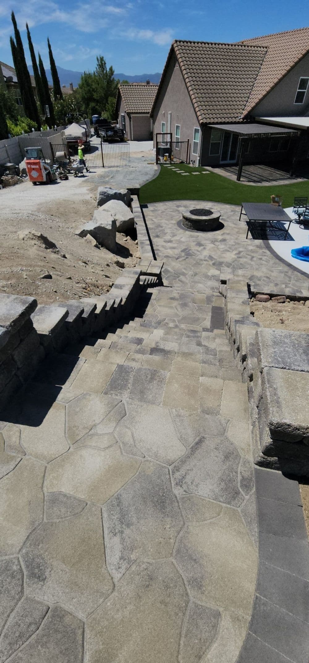 Stone pathway leading down to a backyard with fire pit and pool, surrounded by landscaping.