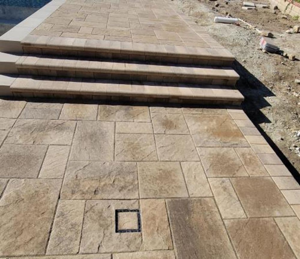 Paved patio with stone steps leading to a pool, featuring textured flooring.