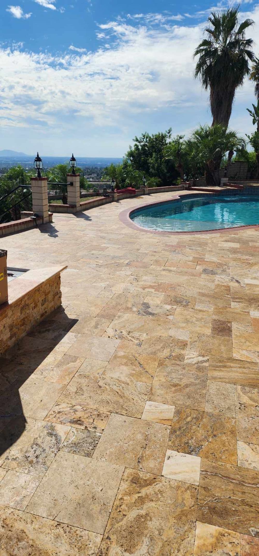 Scenic poolside view with stone patio and palm trees under a blue sky.
