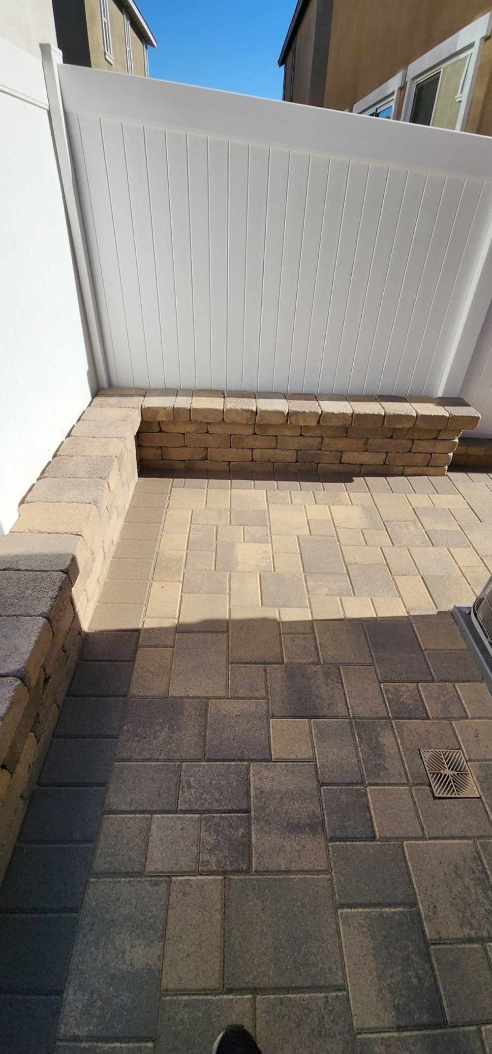 Paved patio area with a white fence and stone seating wall in a residential setting.
