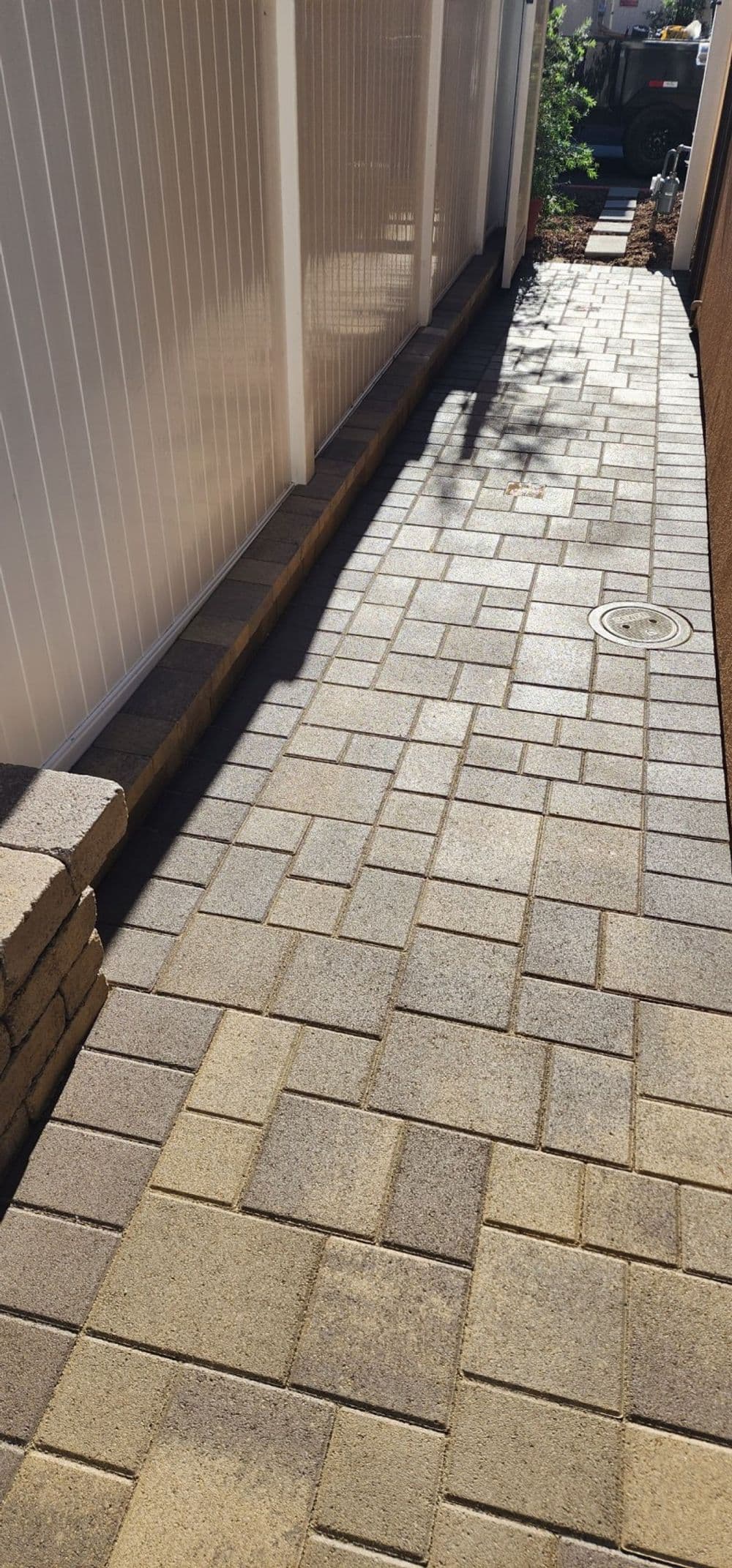 Paved pathway alongside a fence with light and shadow effects.