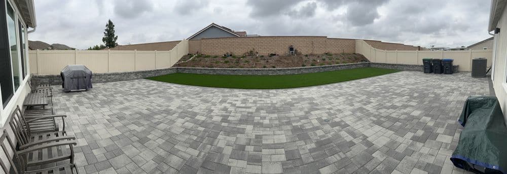 Panoramic view of a landscaped backyard with patio, green lawn, and garden wall.