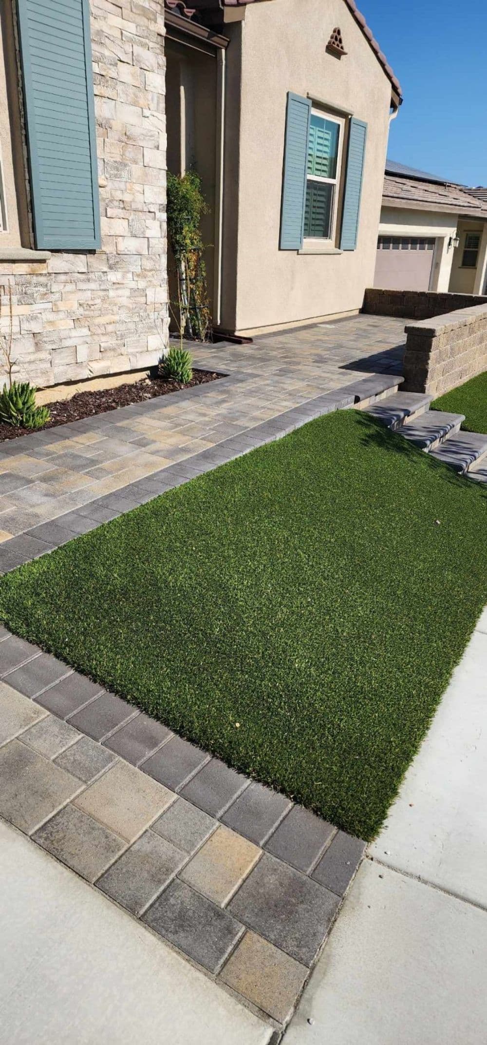 Artificial grass lawn with stone pathway and a light-colored house exterior.