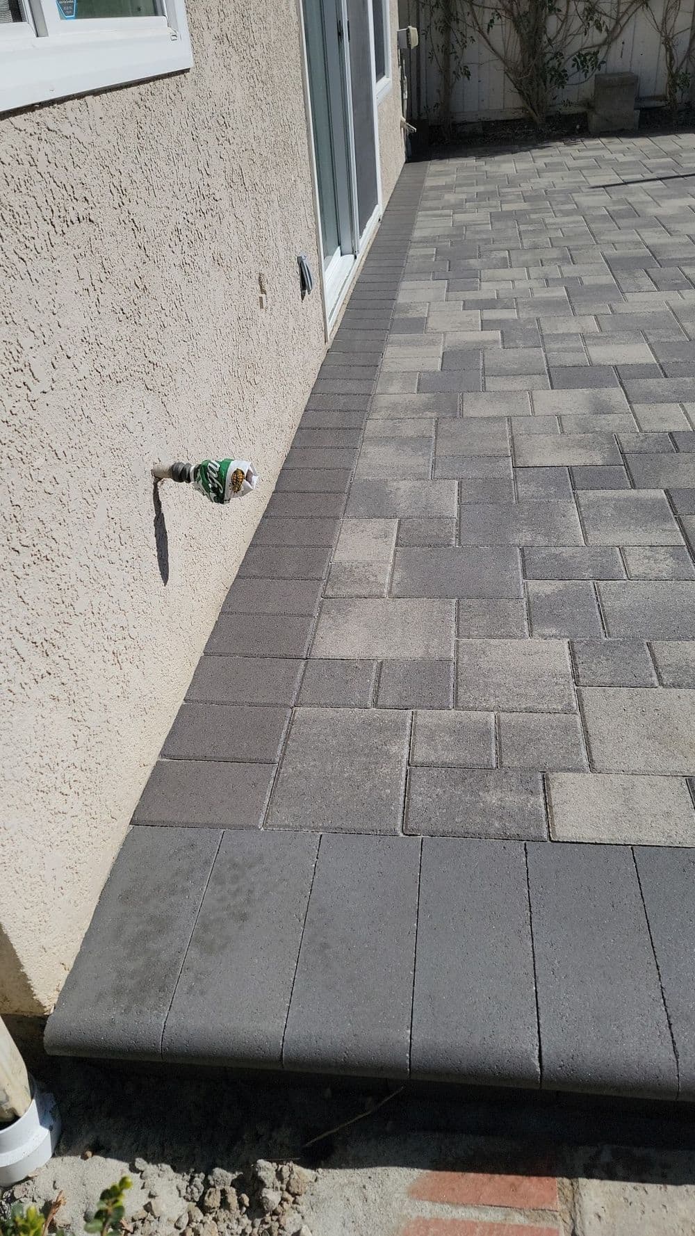 Paved patio area with gray interlocking stones beside a house wall.