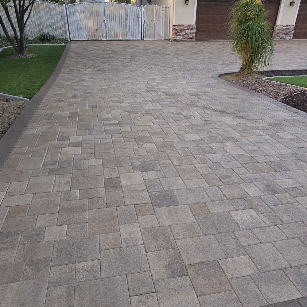 Paved driveway with patterned stones, bordered by grass and palm trees, leading to a garage.