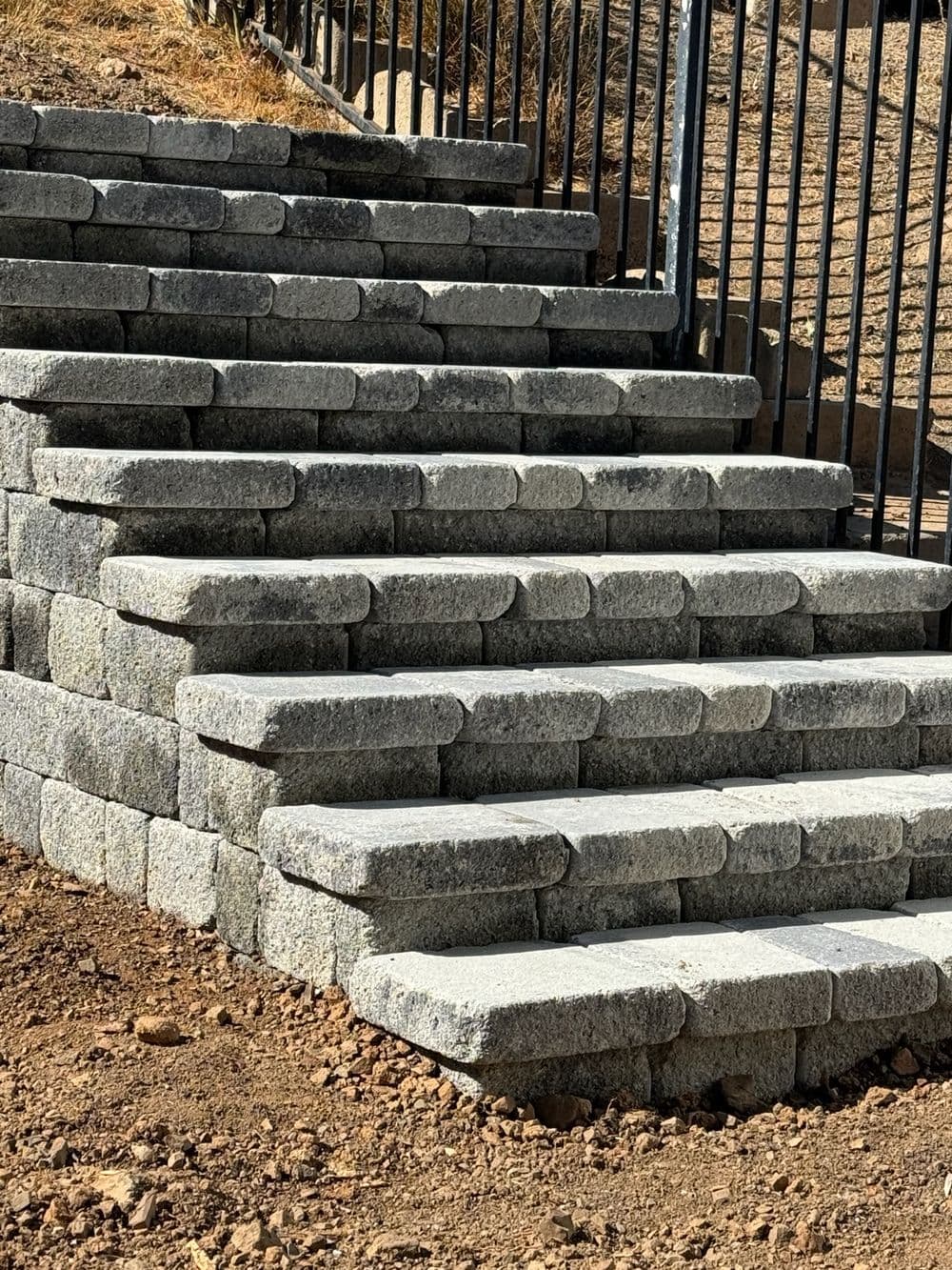 Stone steps made of gray blocks leading up to a gated area, on a gravel surface.