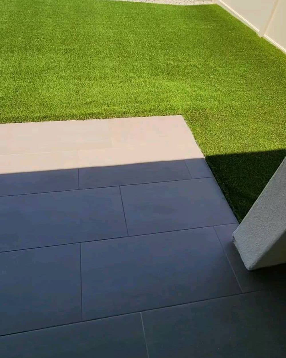View of a patio area with modern tiles leading to a lush green artificial lawn.