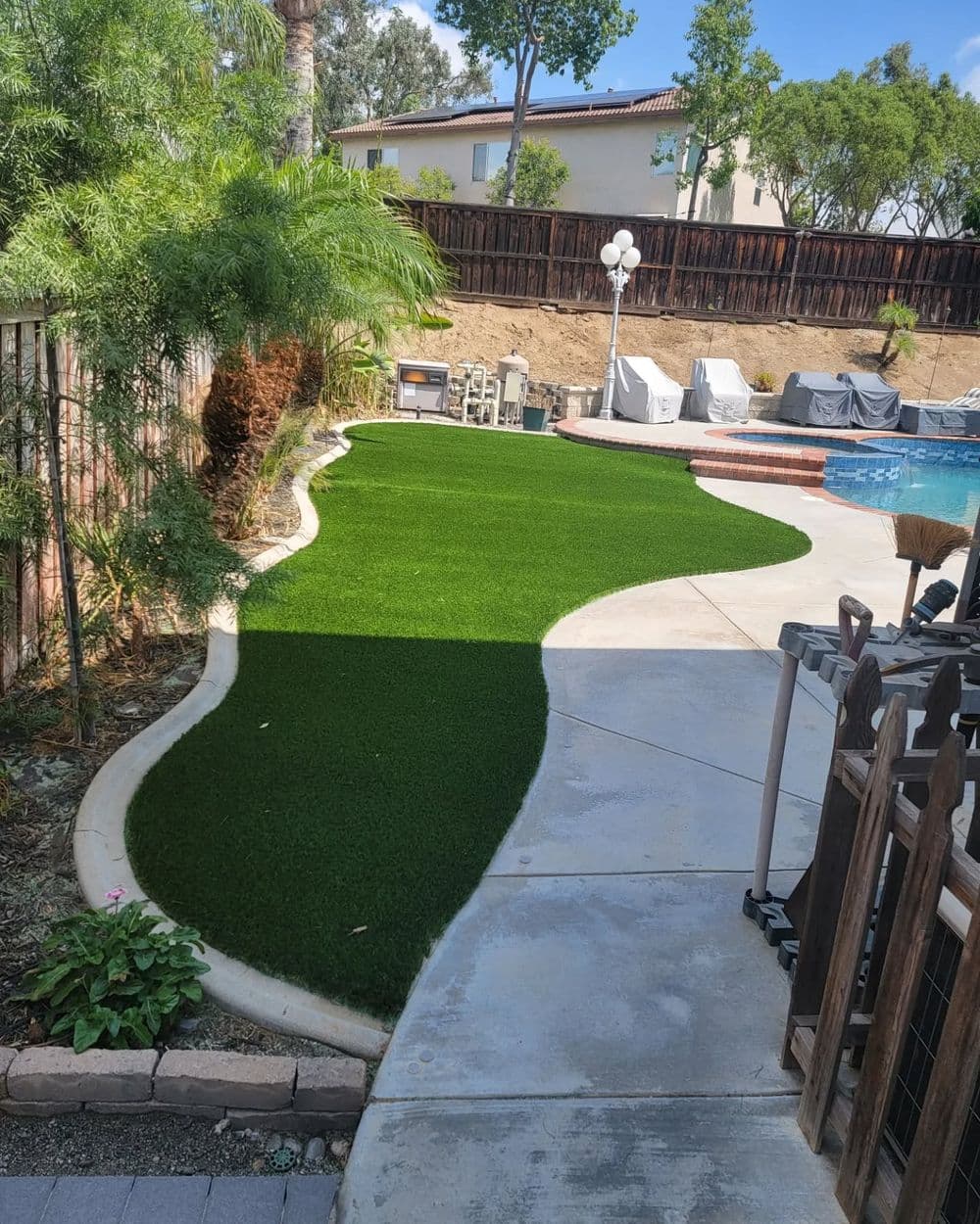 Lush artificial grass lawn curving around a pool in a backyard landscape.