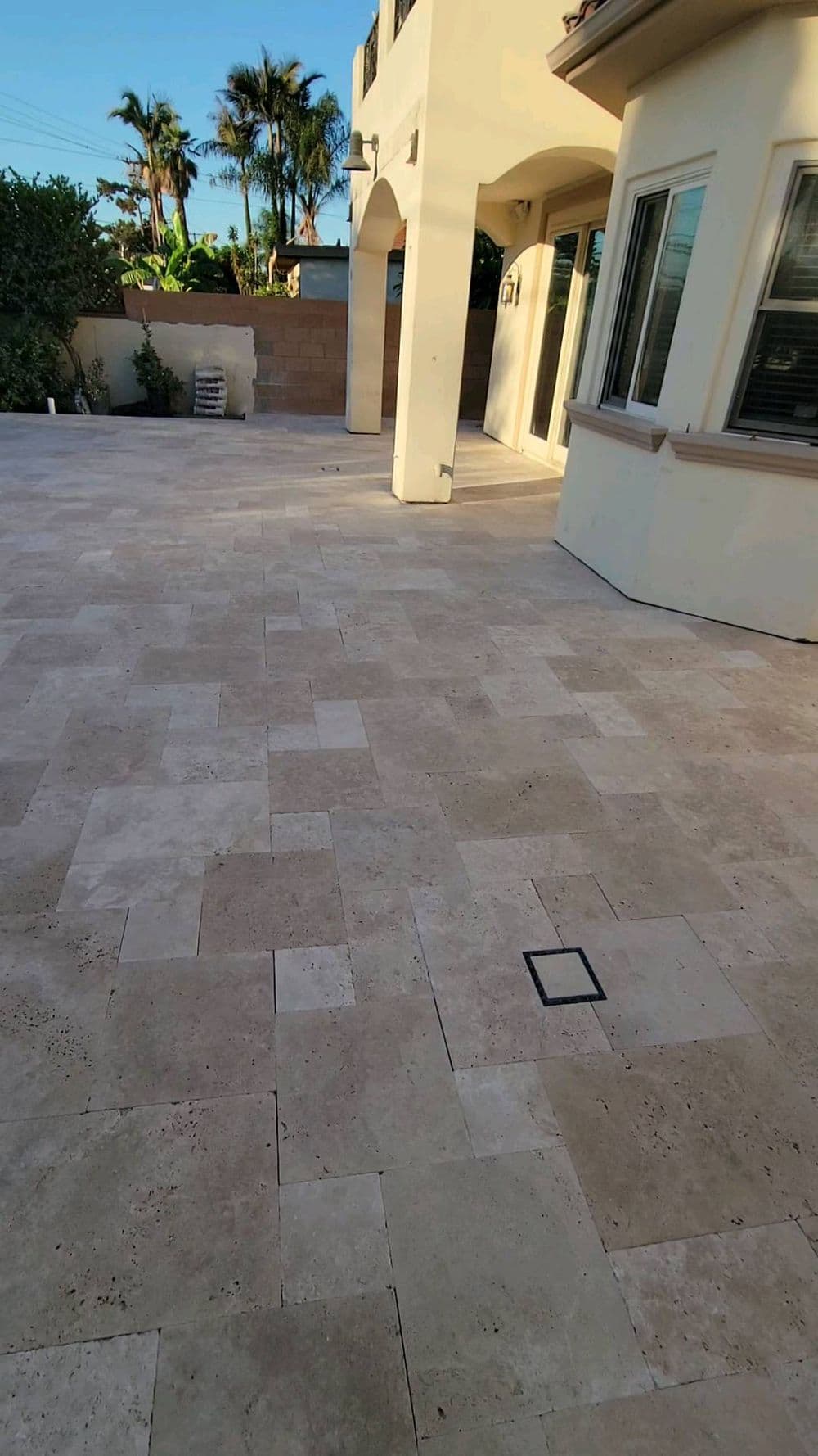 Paved patio area with light-colored stone tiles and palm trees in the background.