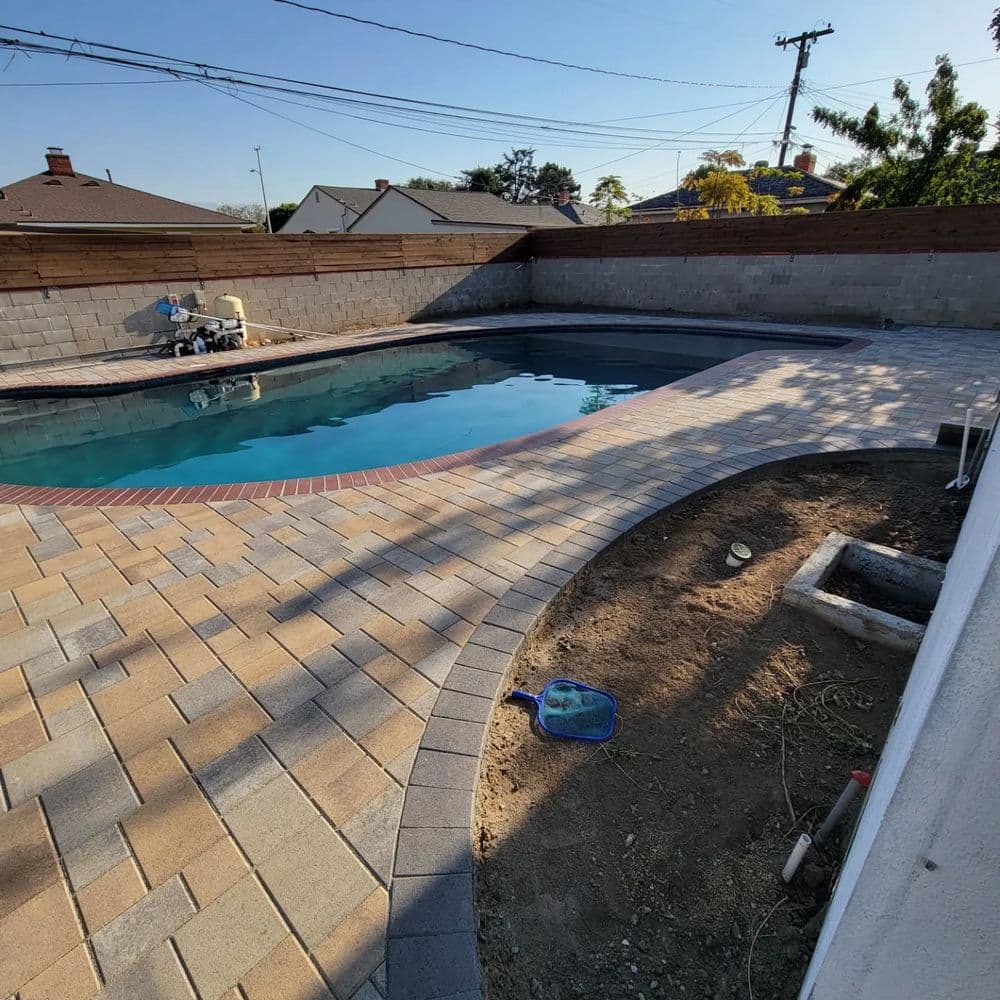 Backyard pool with stone patio and clear water, surrounded by wooden fence and landscaping.