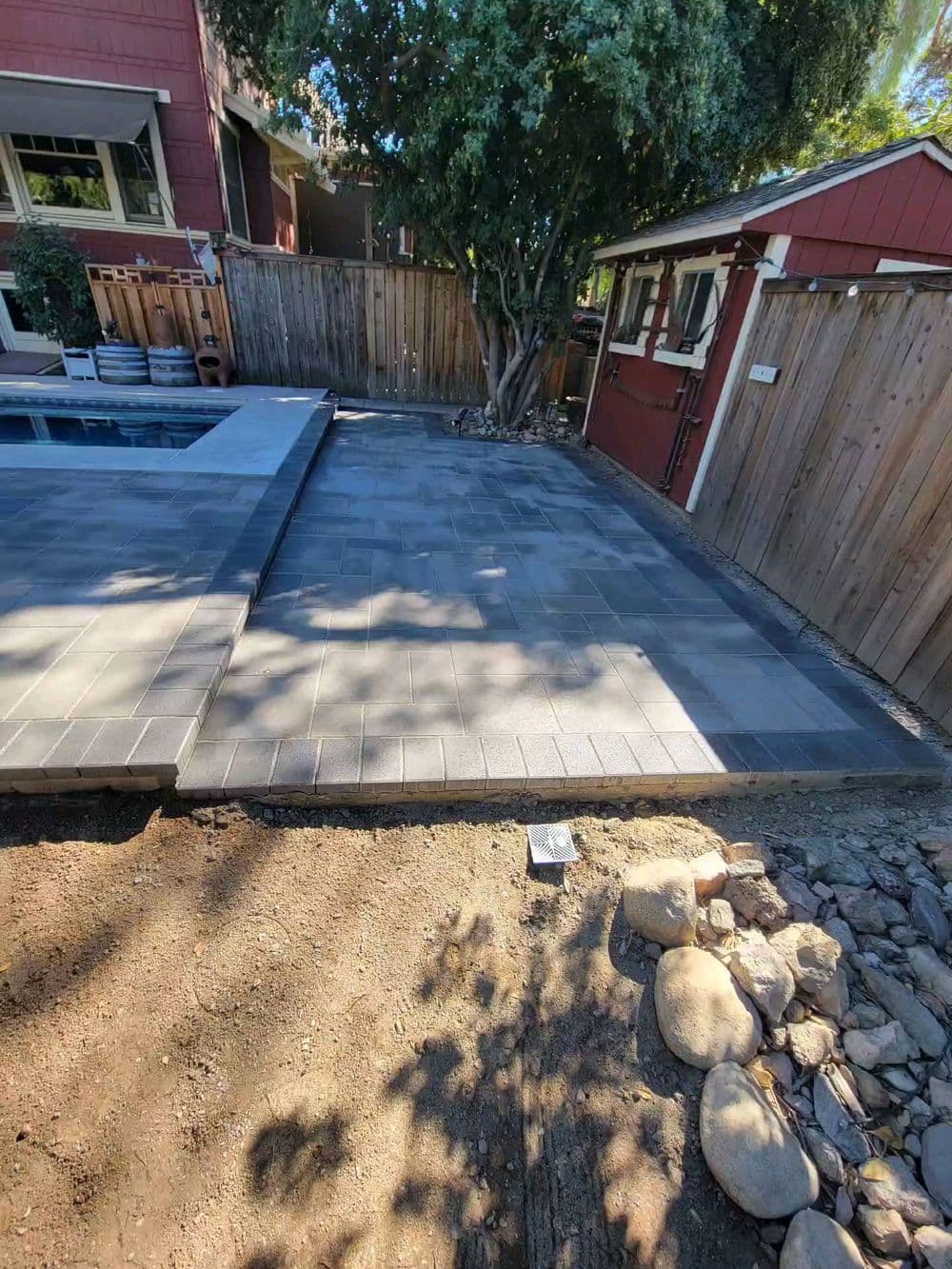 Gray paver patio installed next to a pool and wooden fence in a residential backyard.
