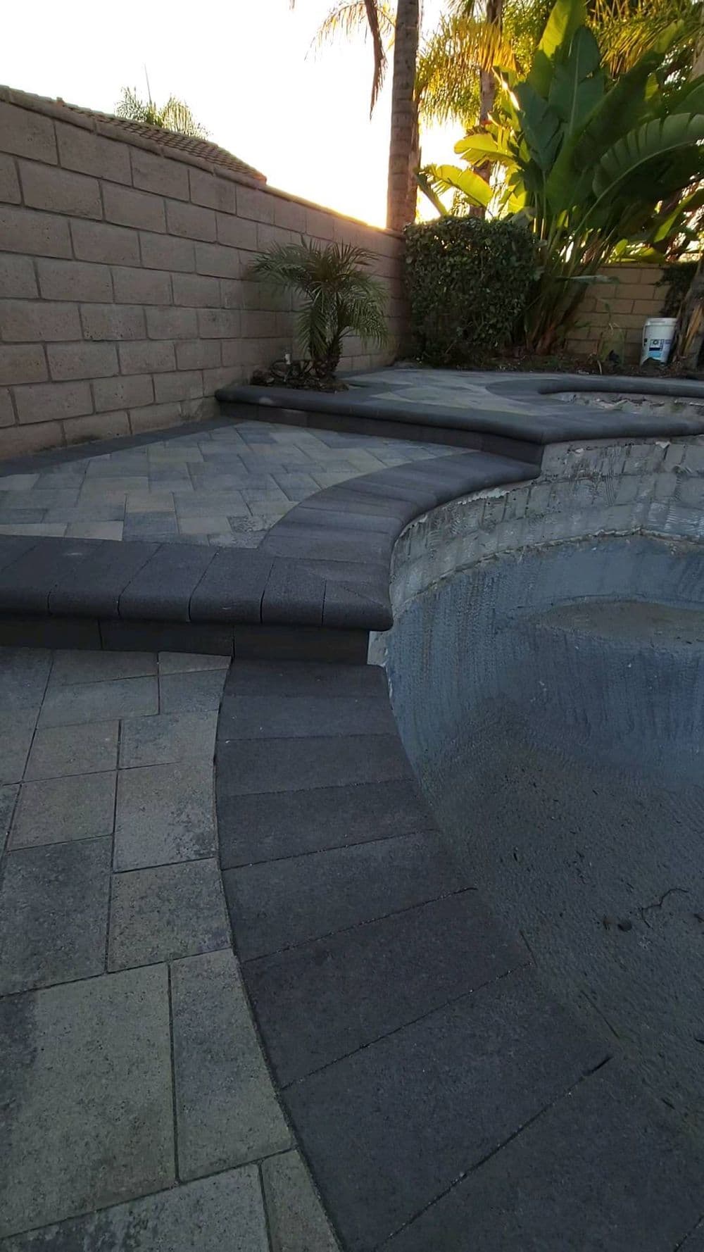 Paved pool area with curved steps and tropical plants at sunset.