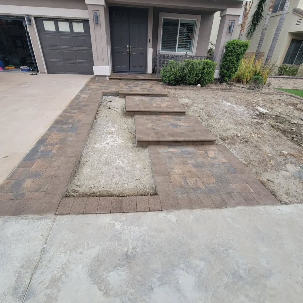 Paver walkway leading to a house with unfinished landscaping and steps.