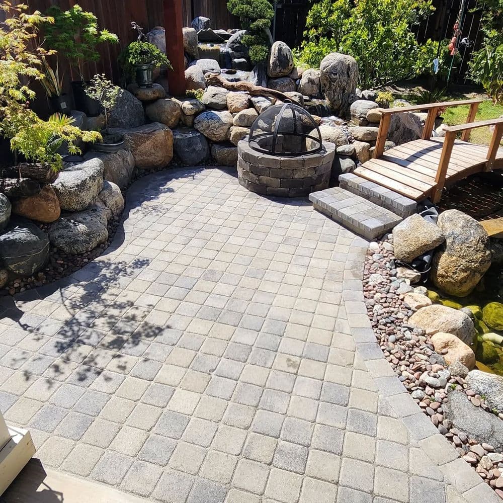 Zen garden with stone pathways, a fire pit, and a wooden bridge over a pond.